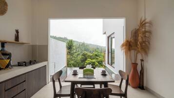 Un comedor con una mesa dispuesta para dos, una barra de cocina y vistas a un paisaje verde exuberante.