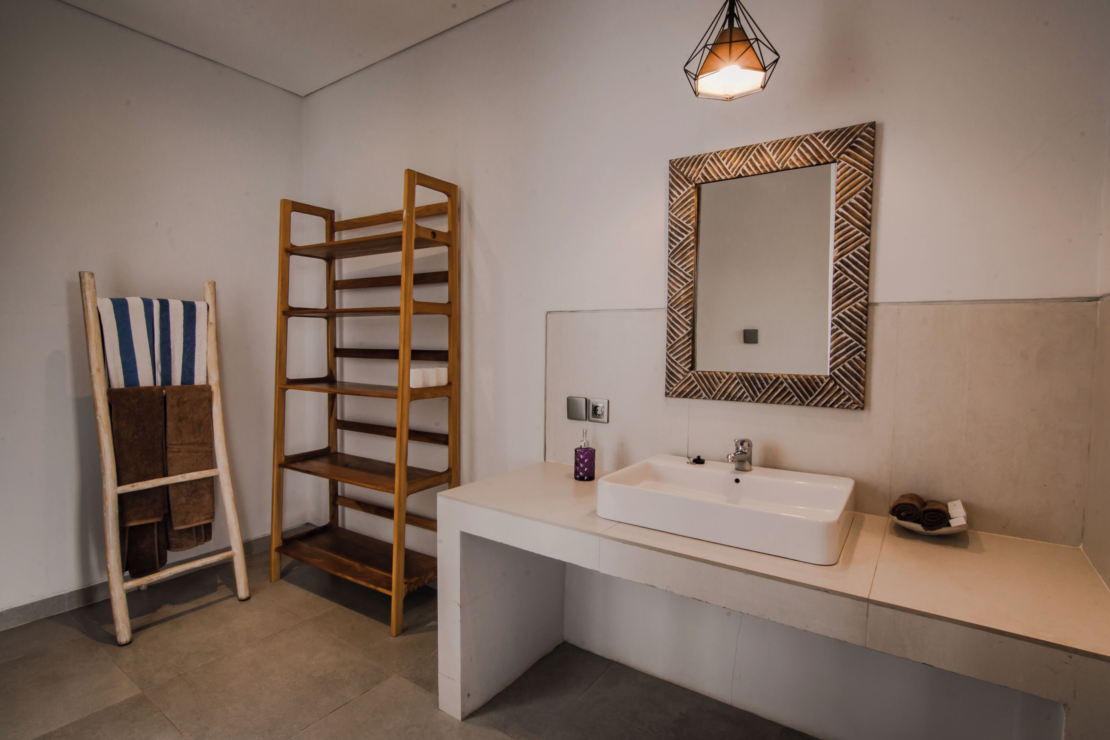 A modern bathroom with a white sink, a mirror with a geometric frame, and a wooden towel rack.