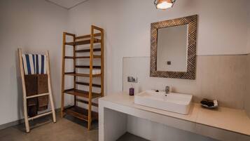 A modern bathroom with a white sink, a mirror with a geometric frame, and a wooden towel rack.