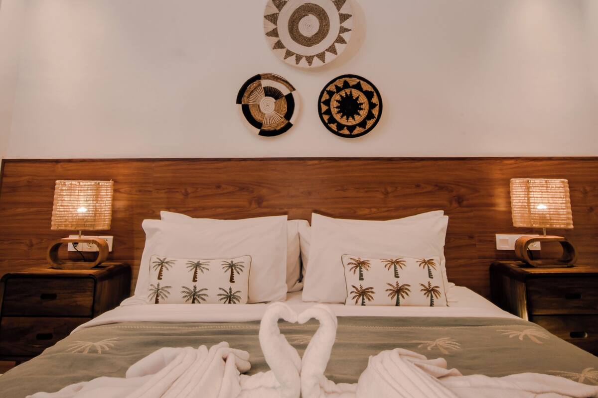 Ein Hotelzimmer mit einem hölzernen Kopfteil, einem Bett mit Schwanen-Handtuch-Arrangement und Wanddekoration mit kreisförmigen und sternförmigen Mustern.