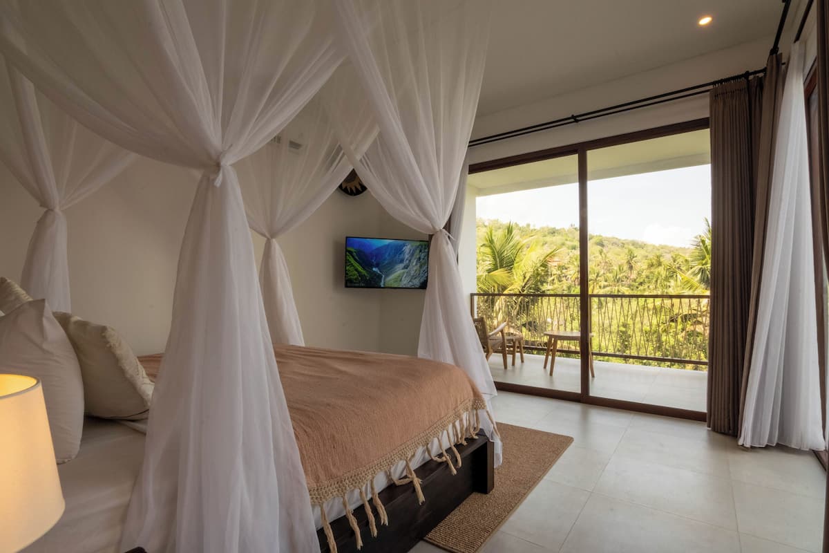Ein Schlafzimmer mit Bett, Vorhängen, Fernseher und einem Balkon mit Blick auf Grünflächen.