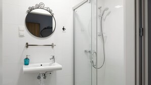 A modern bathroom with a glass-enclosed shower, a white sink with a soap dispenser, and a round mirror with a decorative frame. - MoHo Modern Hostel (Wroclaw)