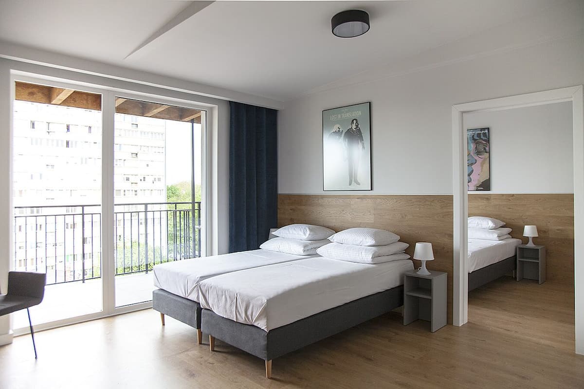 A modern hotel room with a large bed, a small bedside table, a chair, and a balcony with a view of the city.