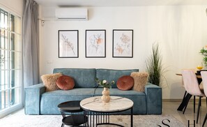 A living room with a blue sofa, a round coffee table, and three framed botanical prints on the wall.