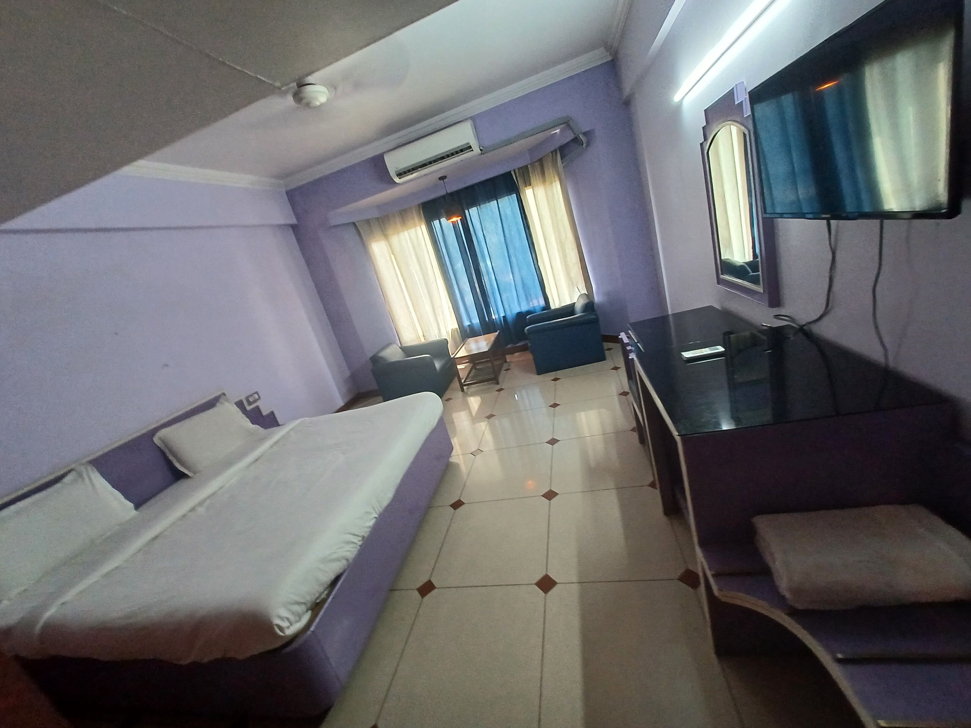 Habitación de hotel con cama, escritorio, silla, aire acondicionado, espejo y ventana con cortinas.