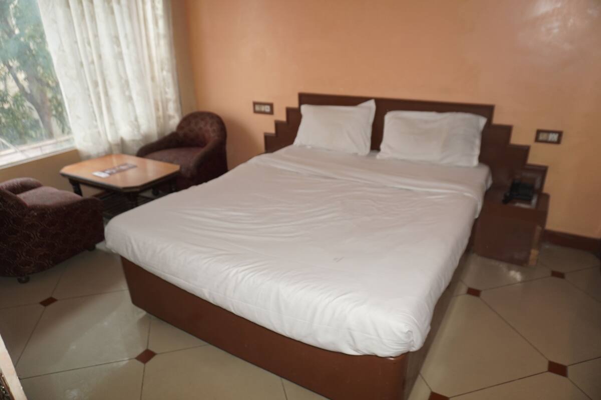 A hotel room with a large bed, a chair, a small table, and a window with curtains.