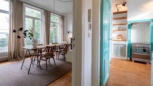 A dining area with a wooden table and chairs, a vase with flowers, and a view through a window with curtains. - The Handshake House by Shway (Antwerpen)