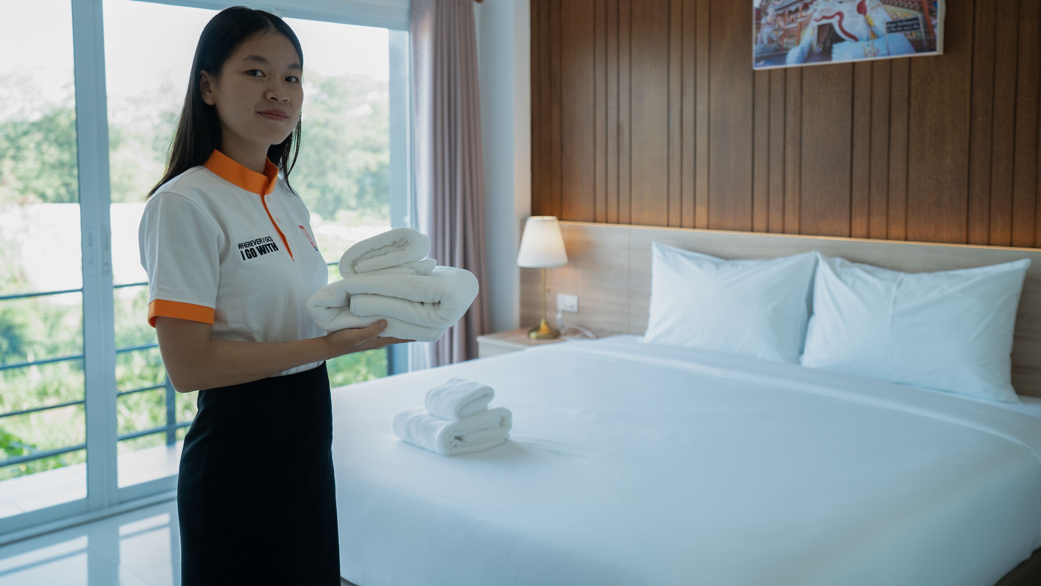A hotel room with a neatly made bed, a nightstand with a lamp, and a window with curtains.