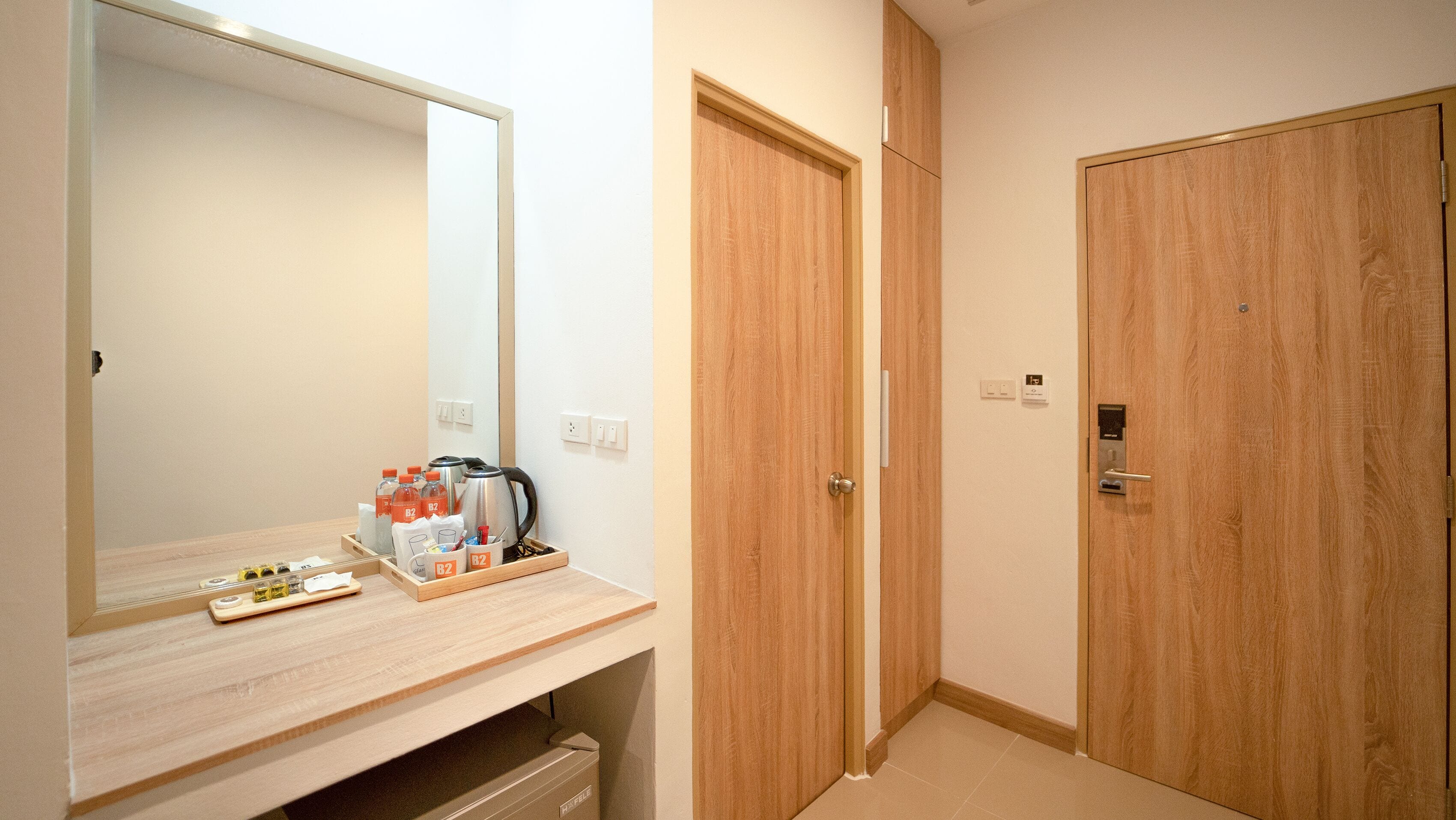 A hotel room with a wooden vanity, a mirror, a tray with toiletries, and two wooden doors.