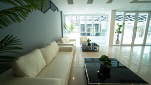 A modern living room with a white sofa, a glass coffee table, and a view of the outdoors through large windows. - B2 Nakhon Sawan Boutique & Budget Hotel (Nakhon Sawan)