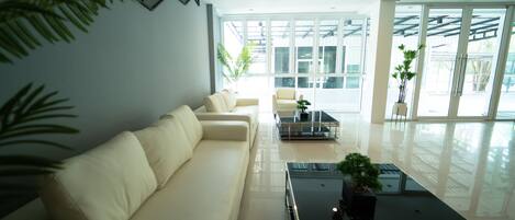 A modern living room with a white sofa, a glass coffee table, and a view of the outdoors through large windows.