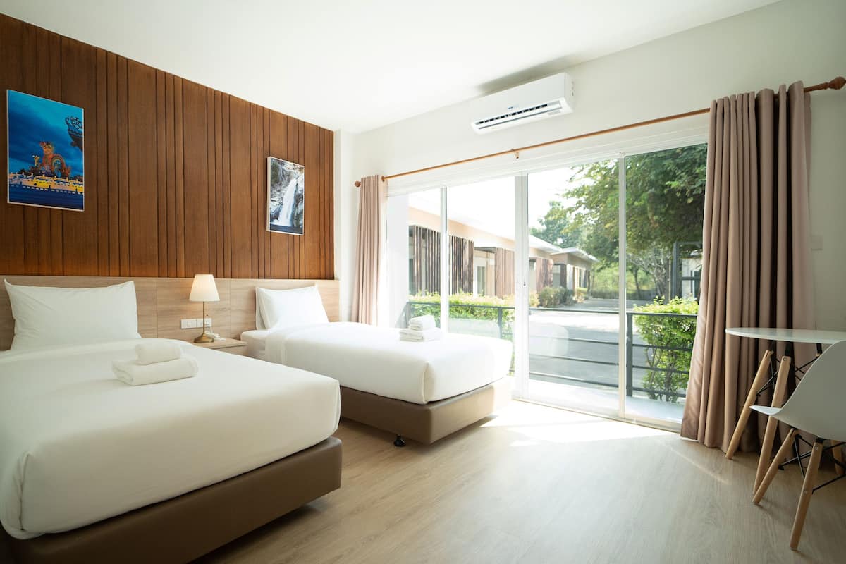 A hotel room with two beds, a desk, and a view of the outside.