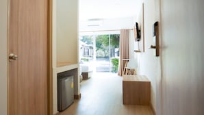 A hallway leading to a room with a bed, a small table, and a chair. There is a refrigerator and a window with curtains. - B2 Nakhon Sawan Boutique & Budget Hotel (Nakhon Sawan)
