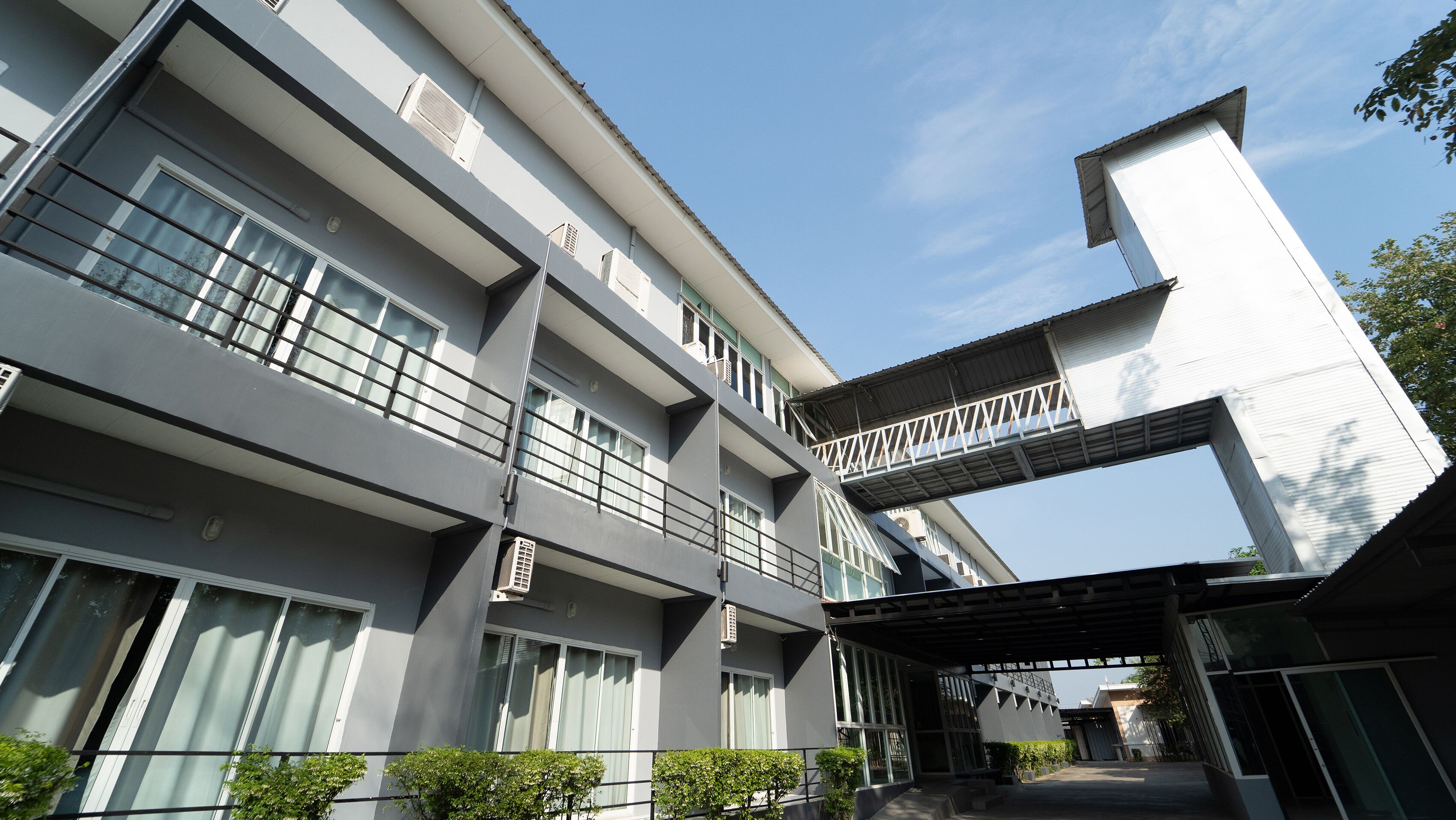 A multi-story building with a modern architectural design, featuring balconies, large windows, and a covered walkway.