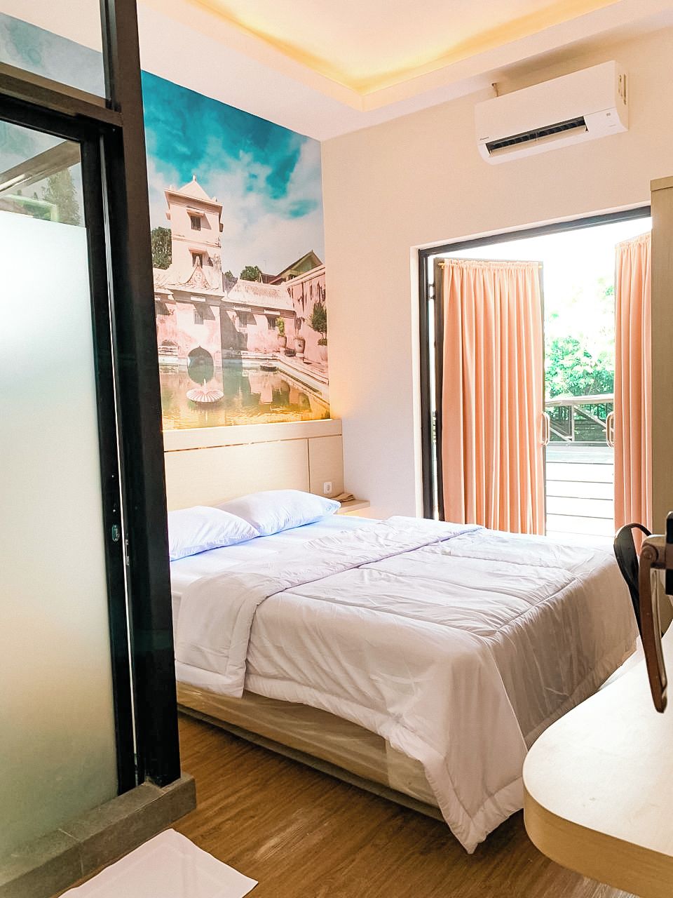 Een hotelkamer met een bed, een raam met gordijnen, een schilderij aan de muur en een plafondventilator.