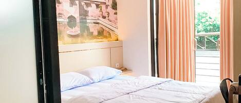 A hotel room with a bed, a window with curtains, a painting on the wall, and a ceiling fan.