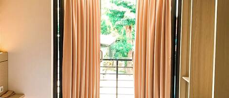 A hotel room with a bed, an air conditioning unit, a wardrobe, and a view of the outdoors through a doorway.