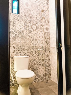 A bathroom with a toilet, patterned tiles, and a shower area. - Kartiko Palagan Eksklusif Yogyakarta (Depok)