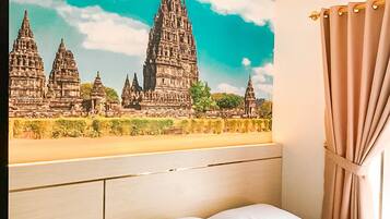 A hotel room with a bed, a chair, a wall-mounted painting of a temple, and a curtain.