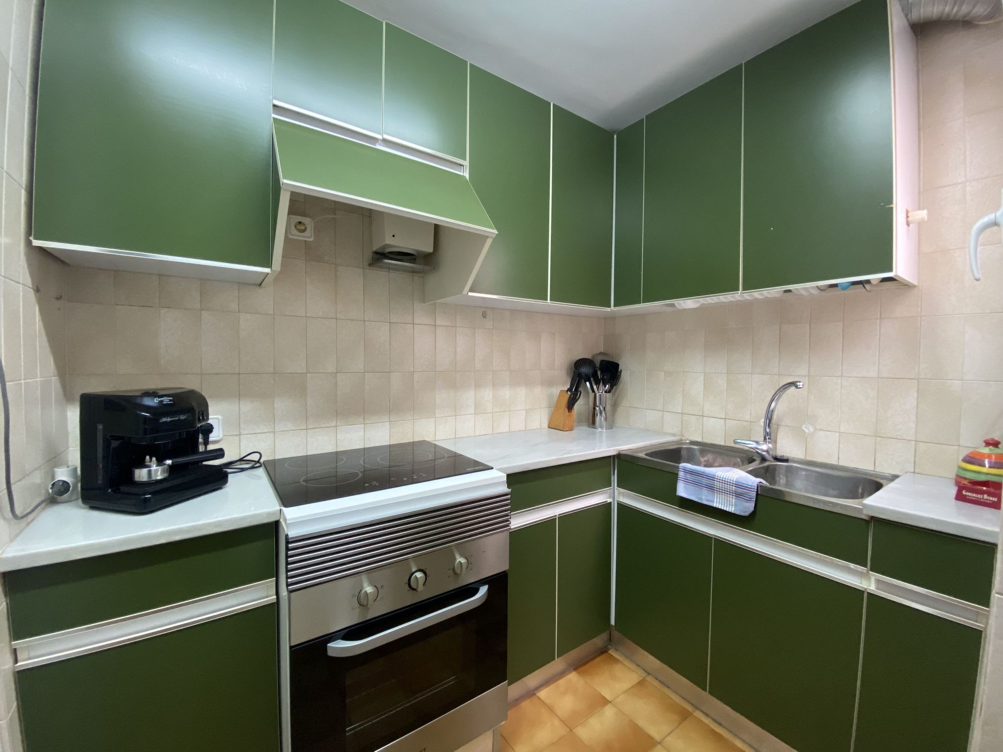 A kitchen with green cabinets, a built-in oven, a stovetop, and a sink.