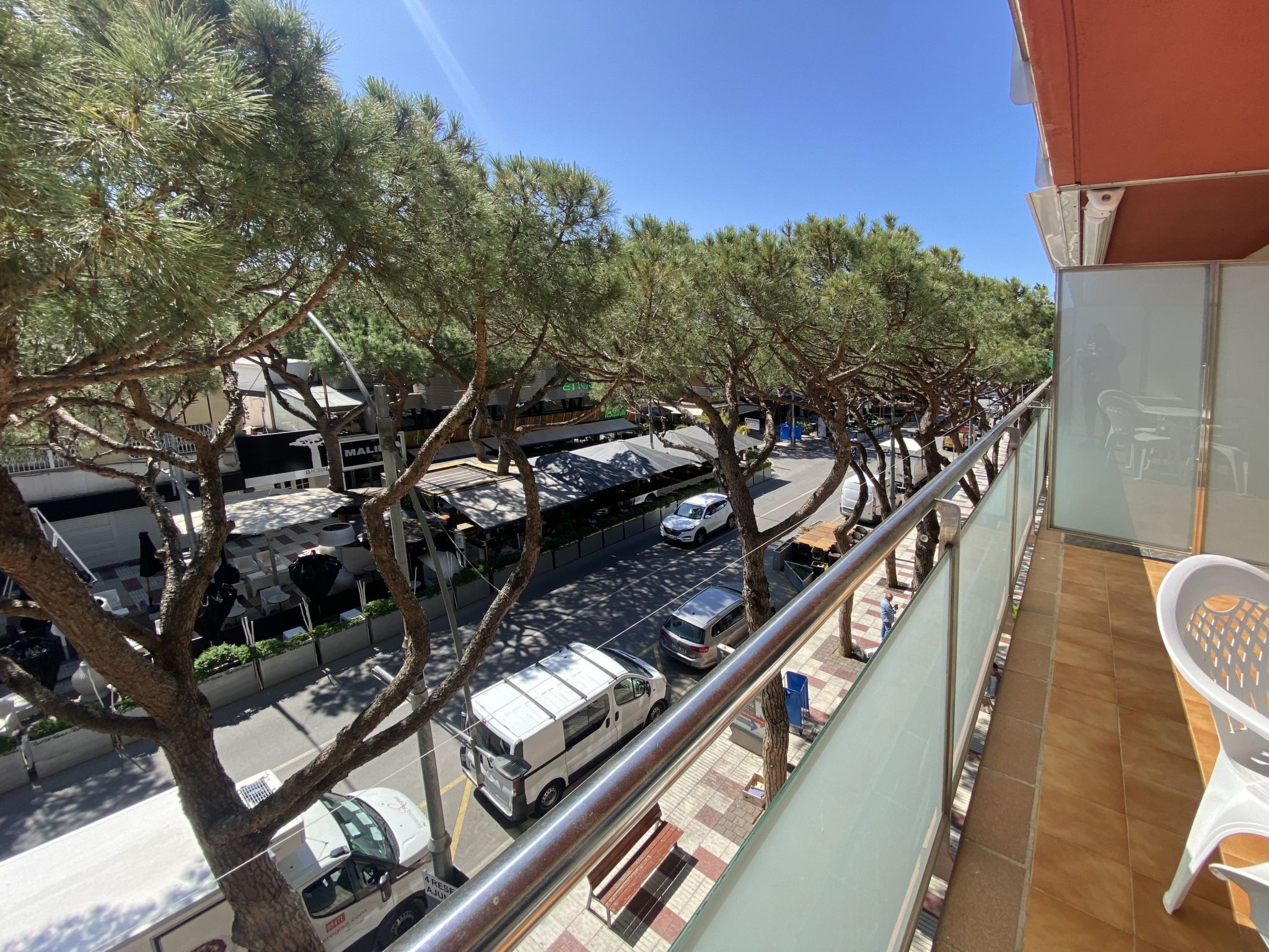 Un balcón con vista a una calle bordeada de árboles y coches estacionados.