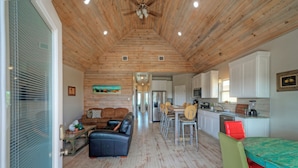 A spacious living area with a wooden ceiling, a dining table with chairs, a kitchen area with cabinets, and a seating area with a sofa and a coffee table. - Bay Haven w/ Shared Boat Dock & Waterfront Pool | Big Trout by AvantStay (Corpus Christi)