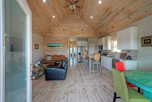 A spacious living area with a wooden ceiling, a dining table with chairs, a kitchen area with cabinets, and a seating area with a sofa and a coffee table.