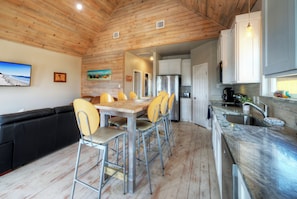 A modern kitchen with a wooden ceiling, a dining area with a table and chairs, and a black sofa.