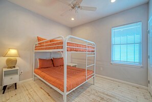 Une chambre avec un lit superposé, un ventilateur de plafond, une lampe de chevet et une fenêtre avec des stores.