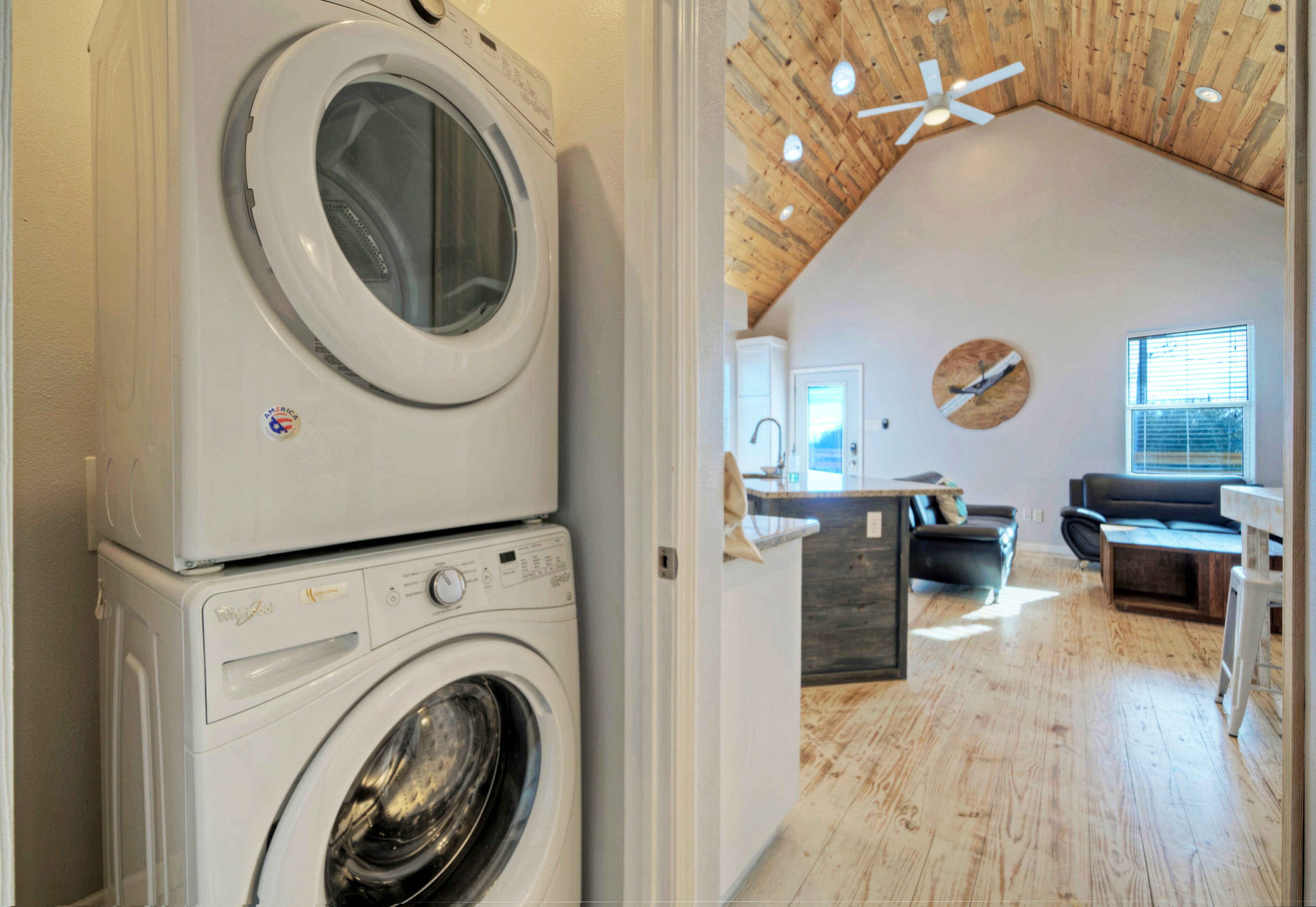Un'area lavanderia con lavatrici impilate, una cucina con elettrodomestici moderni, una zona pranzo con un tavolo in legno e un soggiorno con divano e ventilatore a soffitto.