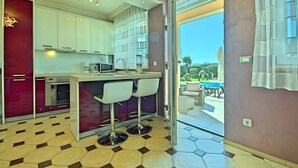 Cocina moderna con gabinetes blancos, una barra con dos taburetes y vistas a un patio exterior con piscina.