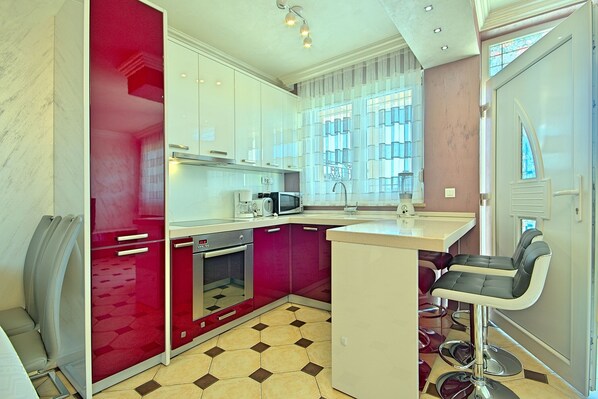 A modern kitchen with red cabinets, a microwave, and a bar stool.