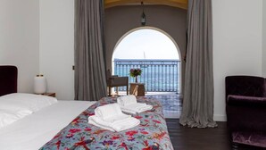 A hotel room with a bed, a chair, a table with a vase, and a view of the sea through an arched doorway. - VILLA DOLCE VITA- 8 bedrooms, sea view, swimming pool, (Ajaccio)