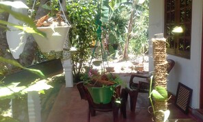 Um quarto iluminado pelo sol com uma porta de vidro, uma mesa de madeira e diversos vasos com plantas.