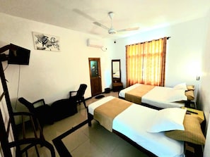 A hotel room with two beds, a desk, a chair, a ceiling fan, and a window with curtains. - Elephant Safari Lodge (Habarana)