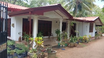 A two-story house with a covered porch, multiple potted plants, and a visible door.