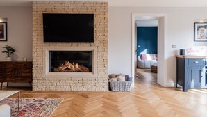 Een woonkamer met een stenen openhaard, een flatscreen televisie erboven en een visgraat parketvloer.