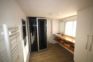 A modern bathroom with a glass shower enclosure, a wooden vanity with copper bowls, and a white sink.