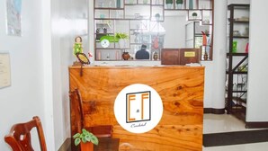 Uma receção com bancada de madeira, um logótipo e vista para a área de cozinha.