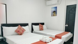 Quarto de hotel com duas camas de solteiro, cada uma com colchão branco e manta vermelha. Um pequeno criado-mudo com tampo de vidro e uma cadeira estão à esquerda das camas. Um quadro está pendurado na parede acima das camas, e um aparelho de ar condicionado está fixado na parede.