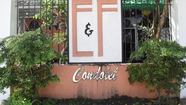 Placa para 'Condotel' com as letras 'EF' em fonte estilizada, cercada por vegetação.