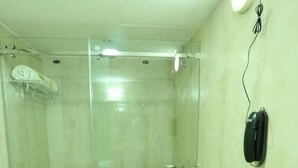 A bathroom with a glass-enclosed shower, a toilet, and a telephone mounted on the wall. - PATTOM ROYAL HOTEL (Thiruvananthapuram)