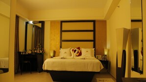 A hotel room with a large bed, a desk, a chair, a mirror, and a TV. - PATTOM ROYAL HOTEL (Thiruvananthapuram)
