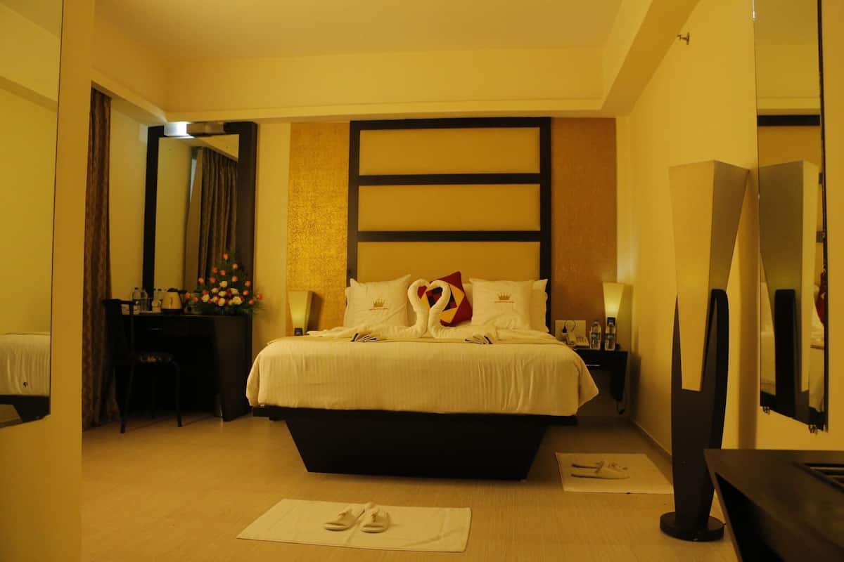 A hotel room with a large bed, a desk, a chair, a mirror, and a TV.