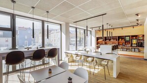 Un caffè moderno con ampie vetrate, tavoli bianchi e sedie nere.