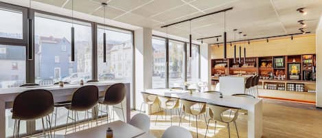 Un caffè moderno con ampie vetrate, tavoli bianchi e sedie nere.