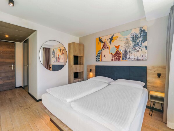 A modern hotel room with a large bed, a round mirror, and a colorful cityscape painting on the wall. - B&B HOTEL Albstadt-Hbf (Albstadt)