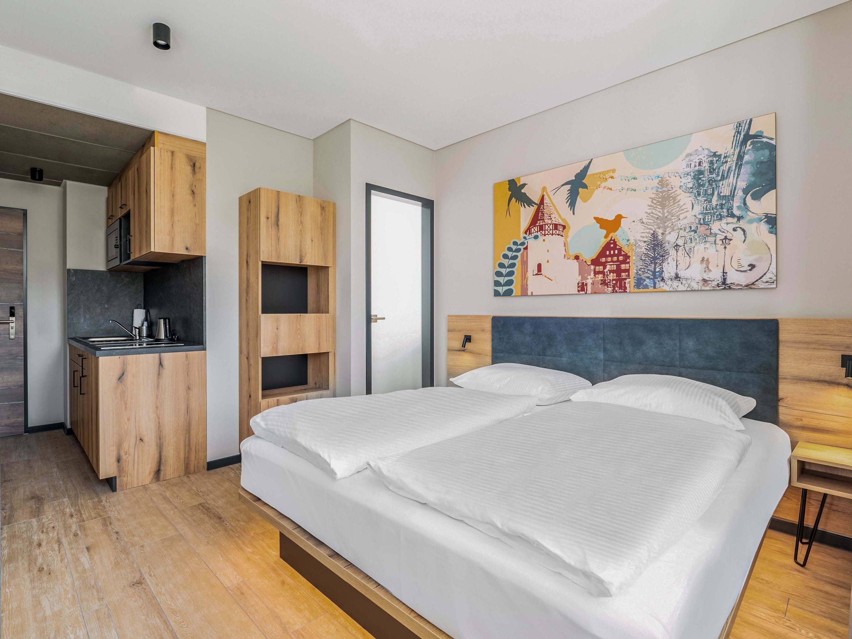 Ein modernes Schlafzimmer mit einem großen Bett, einem eingebauten Schreibtisch und einem farbenfrohen, abstrakten Gemälde an der Wand.