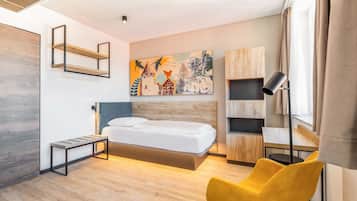 Ein modernes Hotelzimmer mit Holzboden, einem Bett mit Holzfußteil, einem gelben Sessel, einem Schreibtisch mit Lampe und einem Gemälde an der Wand.