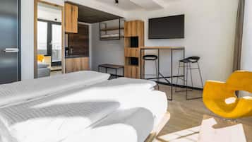 A modern hotel room with a large bed, a desk, a TV, and a yellow chair.